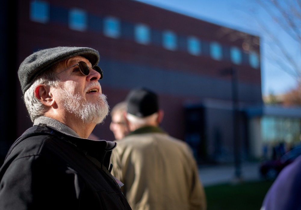 Man with sunglasses and hat on looks up at building